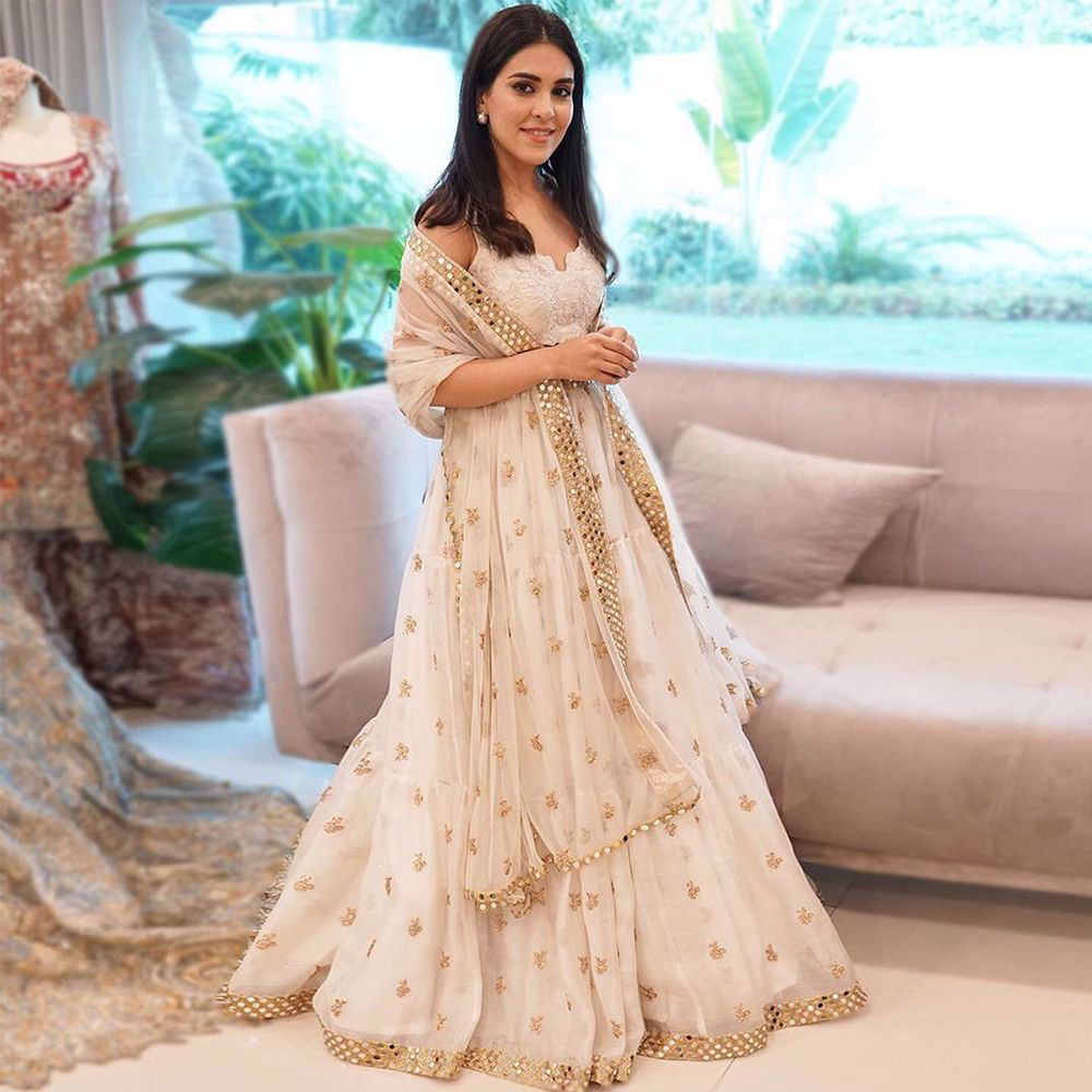 Picture of Aymen Hikmat experiences royalty wearing a beautiful white lehnga choli, with hues of gold, intricately embroidered and meticulously detailed with mirror work highlighting the exquisite craftsmanship of our artisans